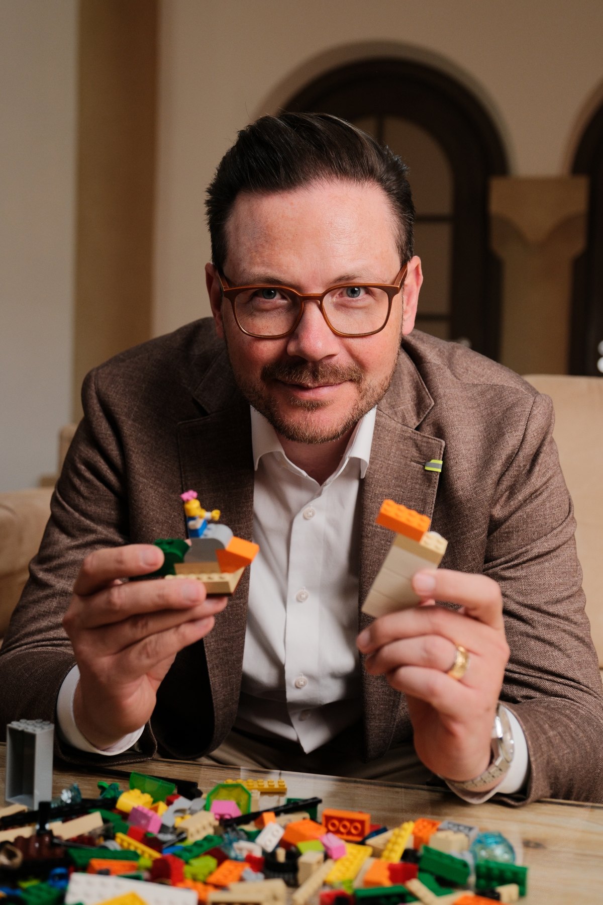 Oliver Gabor hält zwei LEGO Modelle in die Kamera, davor liegen bunte Steine